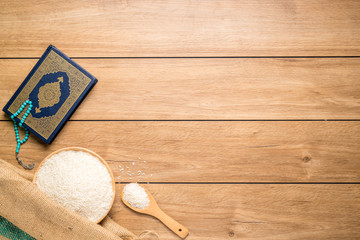 Holy Quran and a grain of rice in a wooden bowl in the sack on a wooden table, Islamic zakat concept. Muslims to help the poor and needy. Conceptual shoot for property, income, and fitrah zakat.