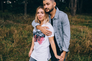 Awsome happy couple have fun in a field sunset background. Handsome Caucasian guy wearing plaid shirt gentle hugs a smiling girl with blond hair in plaid shirt. Lifestyle and travel concept.