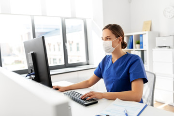 medicine, technology and healthcare concept - female doctor or nurse wearing face protective medical mask for protection from virus disease with computer working at hospital