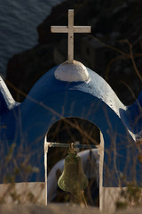 Bell under cross in the ancient chapel on  edge of a cliff over caldera. Santorini orthodox church.