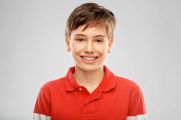 childhood, fashion and people concept - portrait of happy smiling boy in red polo t-shirt over grey...