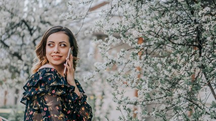 girl talking on the phone on a background of blooming cherry. young girl stands near sakura