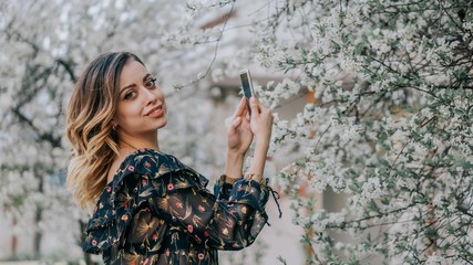 smiling girl photographs a blossoming cherry on a smartphone. young girl takes a selfie near sakura