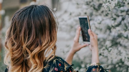 smiling girl photographs a blossoming cherry on a smartphone. young girl takes a selfie near sakura
