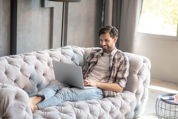 Man in jeans lying barefoot on sofa with laptop.