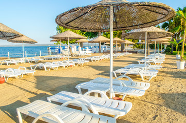 Empty sandy beach at hotel without tourists. Loose white plastic sunbeds. calm blue sea. Summer holiday on coast concept. Vacation background. Holiday backdrop.