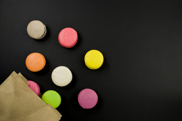 Multicolored macaroons on a black background, top view. Macaroons fall out of a paper bag
