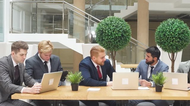 Smart energetic men of different appearance, different nationalities work together as team. Using laptop on working place, business office