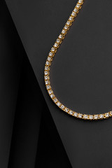 Cropped shot of a golden chain with installed sparkling rhinestones. The part of a luxury collar is isolated on the black fabric surface.