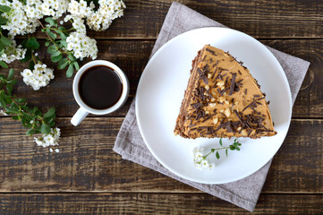 Chocolate cake with nut cream on a wooden table. A piece of cake on a plate and a cup of coffee. The top view