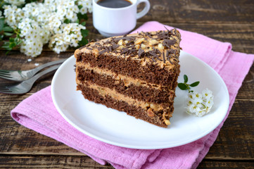 Chocolate cake with nut cream on a wooden table. A piece of cake on a plate and a cup of coffee.