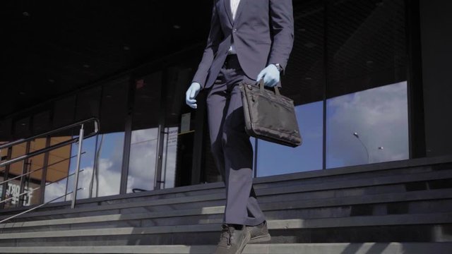 Young business man in suit and medical gloves leaving office with his laptop in black case during pandemic covid-19 coronavirus quarantine. Business is opening after lockdown