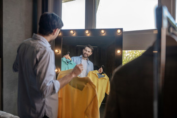 Man reflecting in the mirror with tshirts in his hands