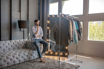Focused man leaning on sofa looking over coat hanger.