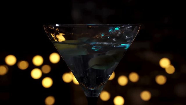 Dropping olives on toothpick and slice of lemon into martini glass filled with transparent drink.