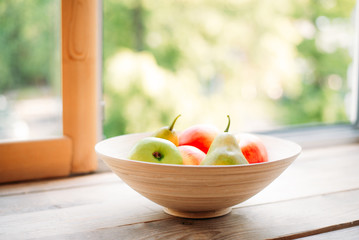 apples and pears on a windowsill in a wooden plate. summer and fresh fruits