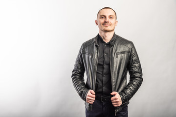 Smiling man in a black shirt and black leather jacket on a light background