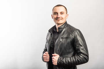 Smiling man in a black shirt and black leather jacket on a light background