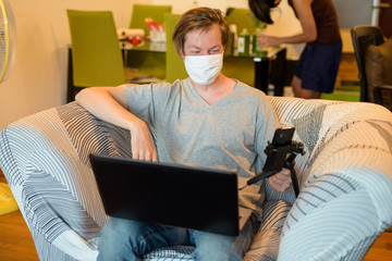 Fototapeta na wymiar Young man with face mask using laptop while vlogging in quarantine at home