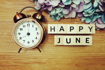 Happy June alphabet letters with alarm clock on wooden background