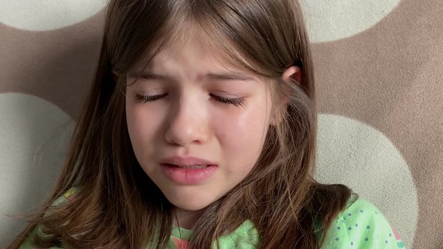 Little girl crying at home on the couch, tears on her face, closeup portrait