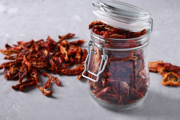 Dried tomatoes with a glass jar on a gray concrete background. Horizontal format