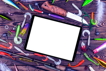 Fishing rod, tackles and fishing baits, reel on wooden board background with tablet computer isolated white screen. Empty space for text