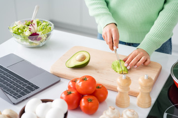 Obraz na płótnie Canvas Cropped photo of housewife hold knife cutting fresh avocado mixing salad ingredients cooking tasty vegan meal look online recipe stand kitchen indoors casual clothing
