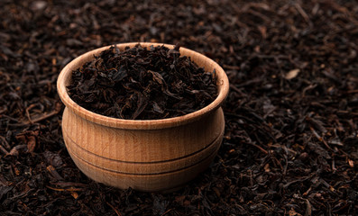 Dry tea leaves in wooden bowl isolated on dark background