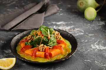 Green radish carpaccio on a black plate with orange sauce, with spinach salad, thinly sliced carrots, apples and walnuts, with slices of red oranges. Tasty and healthy food.