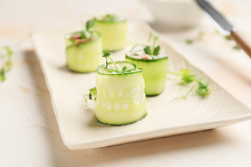 Plate with tasty cucumber rolls on table