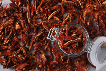 Dried tomatoes in a glass jar on the table against the background of scattered tomato chips. Top view.
