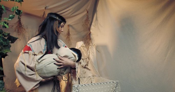 Indian woman in wigwam is holding and rocking her child, 4k