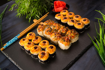 Set of baked sushi rolls with wasabi and ginger on a black background. Japanese oriental cuisine