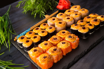 Set of baked sushi rolls with wasabi and ginger on a black background. Japanese oriental cuisine