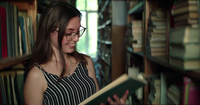 Girl in glasses and teeth braces rejoices when reading book in a library