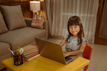 happy little girl doing homework using laptop at home