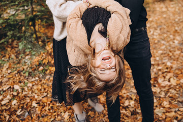 Stylish family in the autumn forest. Models. A young guy and a girl stand on a forest road among yellow leaves and hold their daughter in their arms.