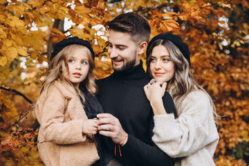 Stylish family in the autumn forest. Models. A young guy and a girl stand on a forest road among yellow leaves and hold their daughter in their arms.