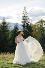 The bride herself poses on a background of mountains. A woman develops a dress in the wind.