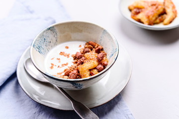 Healthy breakfast yogurt bowl with granola and caramelized bananas and nuts on grey concrete background. Selective focus