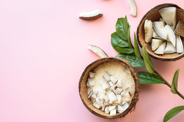 Coconut cut into pieces, coconut shavings, a branch of green leaves lies on a pink background. View from above. Place for text. Flat lay