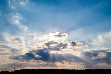 Light blue and pink sky with white and grey clouds before the rain. Sun shining behind the clouds. Nature protection concept. Sunny day, warm weather.