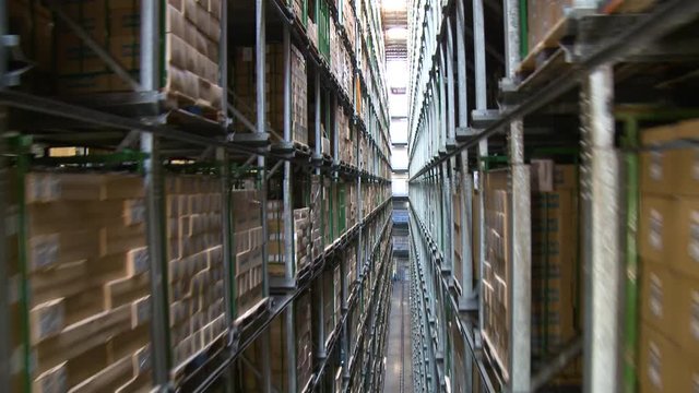 Camera movement through shelves in a warehouse. Cartons are visible on the right and left. 