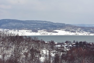 frozen lake in winter season close to the village with forest reflecting in water