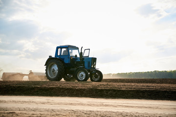 Agricultural work on field with black soil. Blue tractor riding and seeding countryside. Rural works in spring. Environmental protection concept. Ecological products cultivation. Natural background.