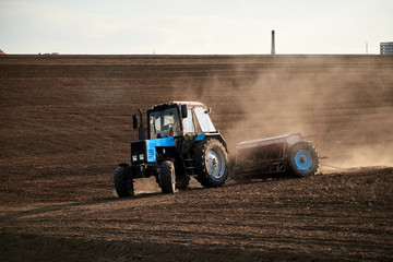 Obraz premium Agricultural work on field with black soil. Blue tractor riding and seeding countryside. Rural works in spring. Environmental protection concept. Ecological products cultivation. Natural background.