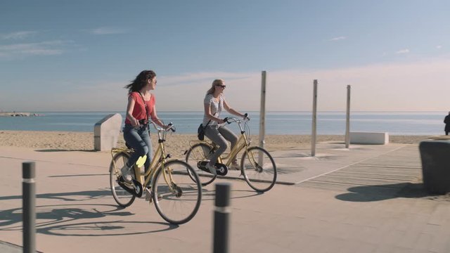 Young Adult female Tourists having fun on bicycle on beach in summer with a motion responds animation