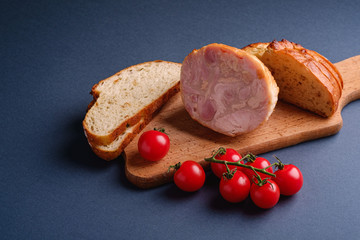 Turkey ham meat, fresh cherry tomatoes branch and loaf sliced bread on wooden cutting board, blue minimal background, angle view, copy space