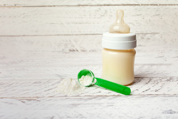 .Baby bottle with milk formula on a white wooden background with empty place for text. Milk powder for the baby. Artificial nutrition of a newborn.